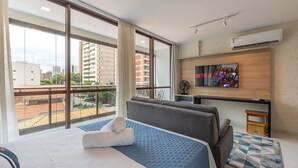 Een hotelkamer met een groot bed, een aan de muur bevestigde televisie en een stadszicht door grote ramen.
