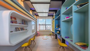 Een kinderspeelkamer met gebogen schapenkasten, gele stoelen en een groot raam.