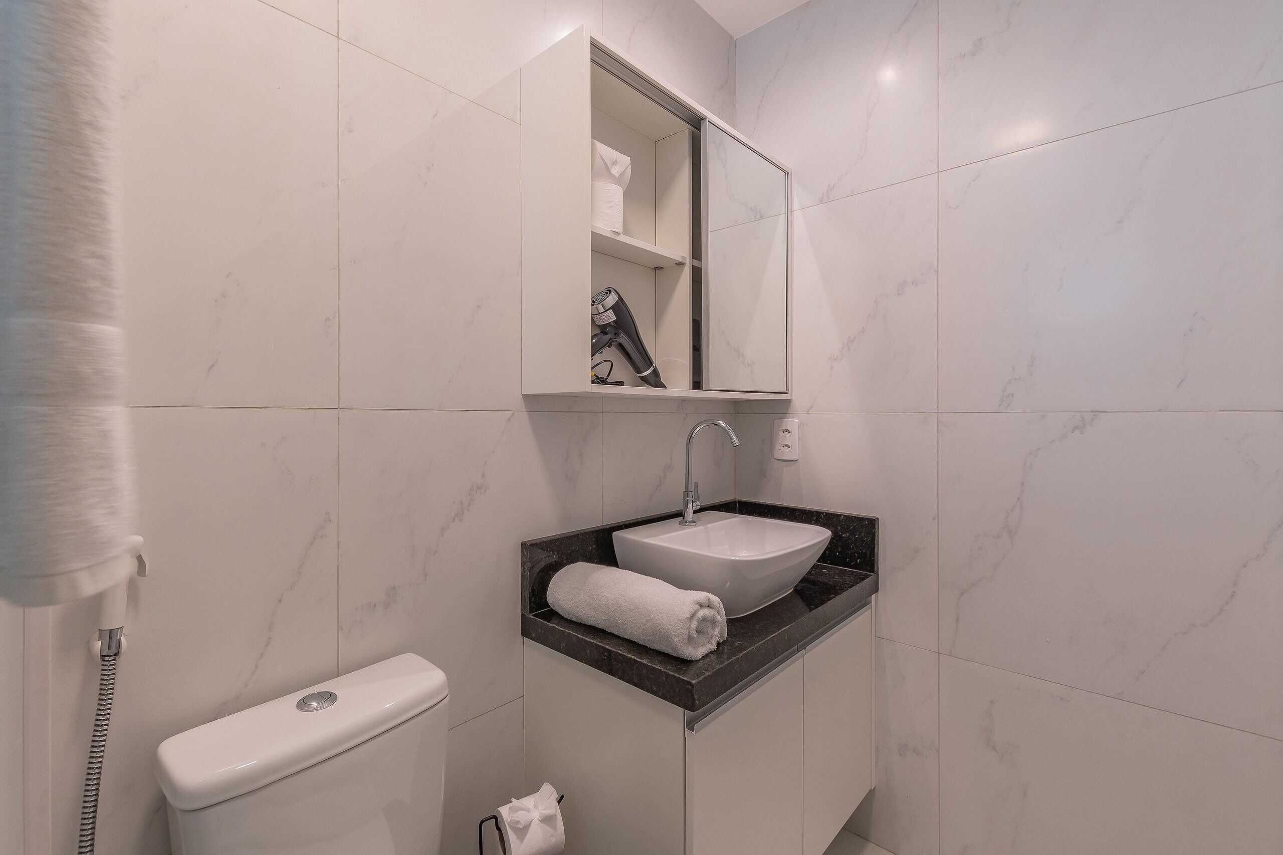 Une salle de bain avec des toilettes blanches, un lavabo doté d’un plan de travail en marbre et un miroir au-dessus du lavabo.