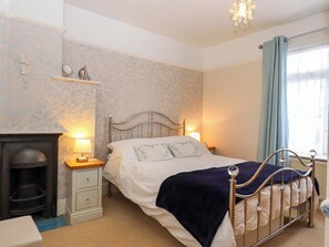 Un dormitorio con cama, lámparas de noche, mesita de noche, cómoda, chimenea y ventana con cortinas.