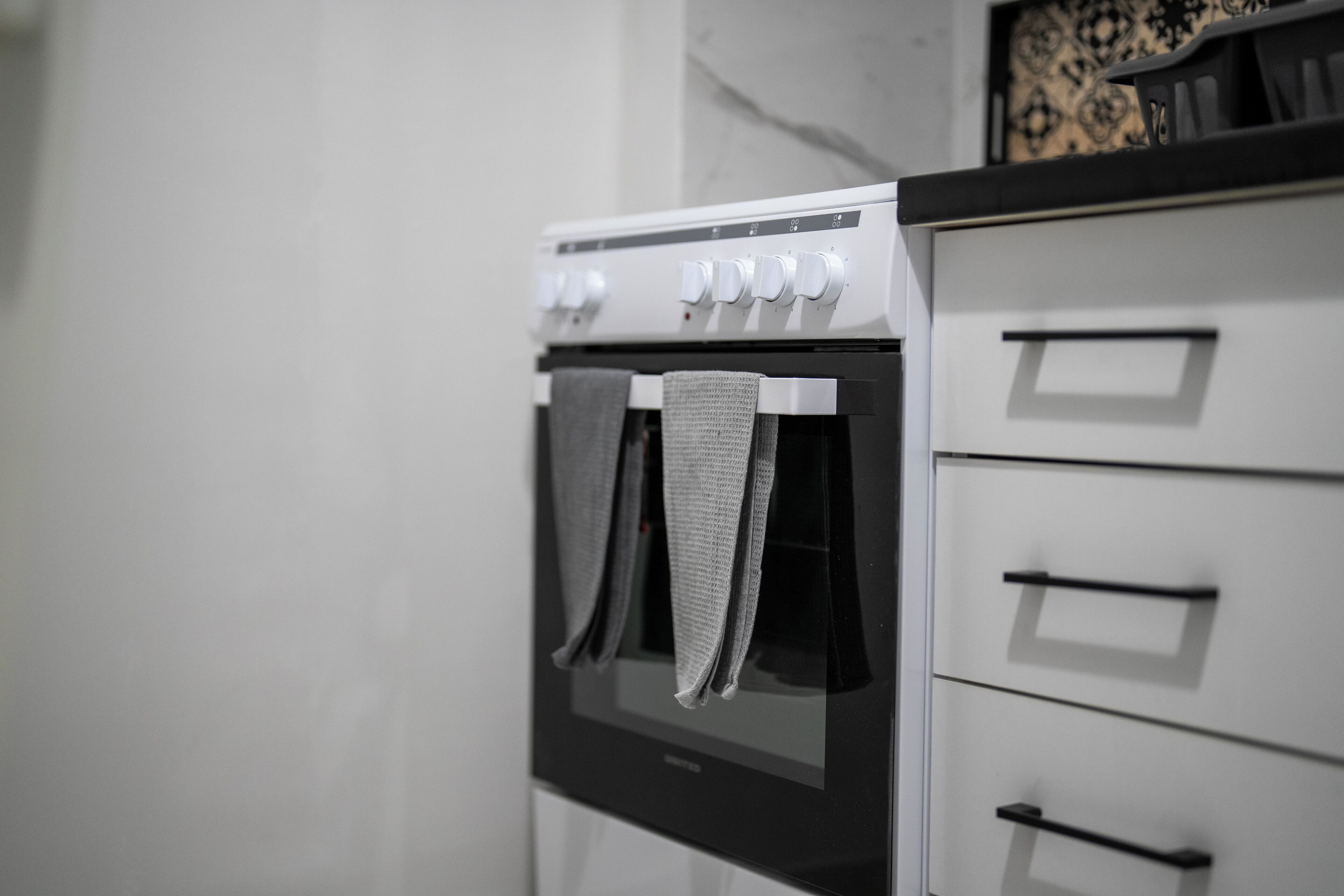 A kitchen with a built-in oven and a white cabinet with black handles.