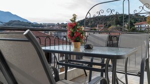 A glass-top table with metal chairs and a decorative plant on a terrace with a view of a town and mountains. - Del Sol 6 Meteora Luxurious Family Suites (Kalampaka)