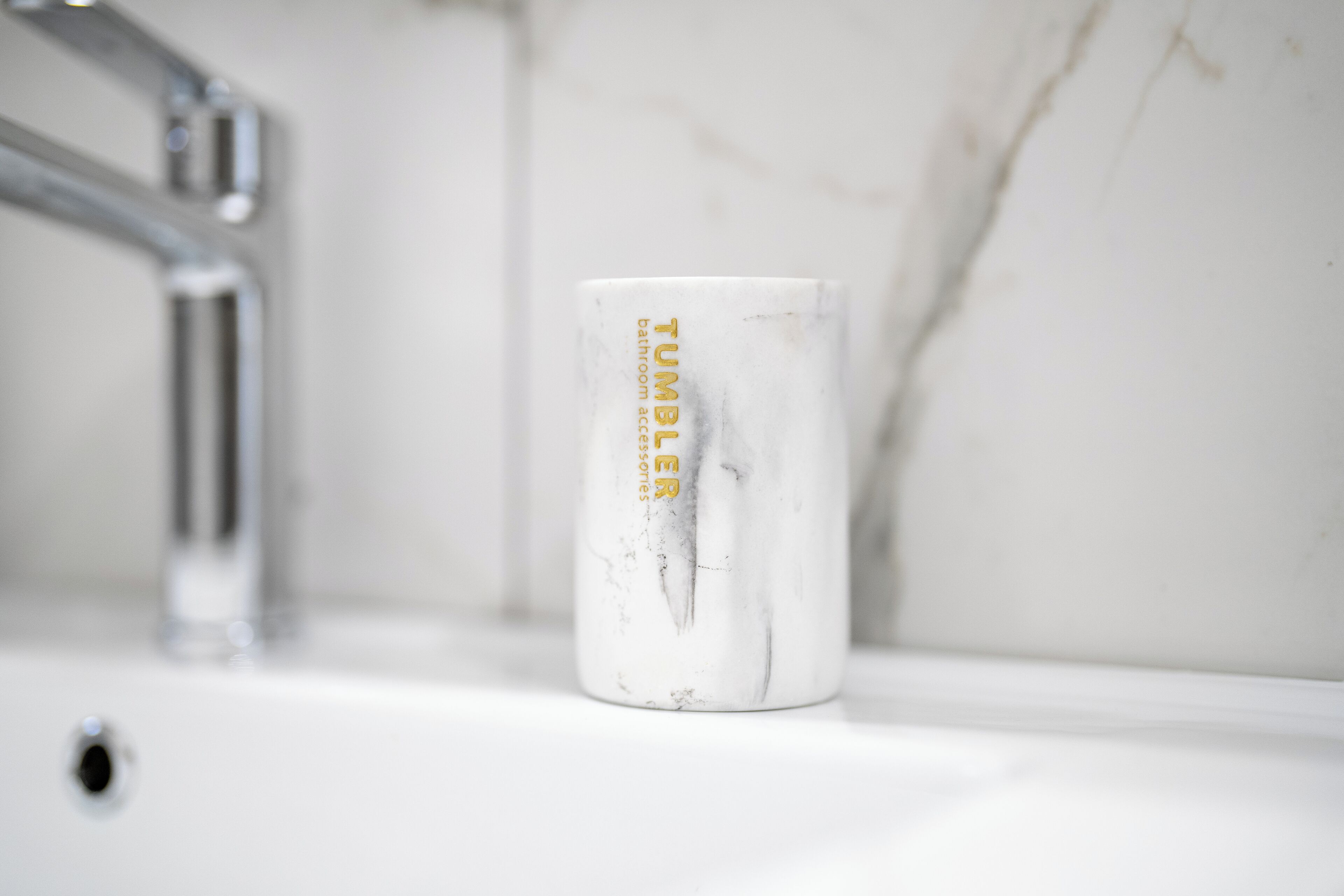 Ein Waschbecken mit weißer Marmorplatte und einer weißen Keramiktasse mit goldener Schrift.