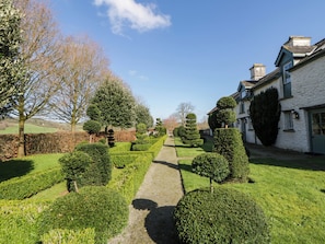Un chemin de jardin bien entretenu mène à un bâtiment traditionnel, peint en blanc et doté d’une façade en pierre.