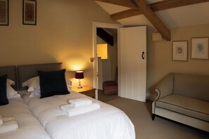 A hotel room with a bed, a bedside lamp, a chair, and a door leading to another room. - North Cottage (Llandovery)