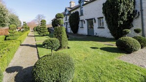 A white building with a traditional design, surrounded by well-maintained hedges and a clear pathway. - North Cottage (Llandovery)