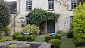 A stone building with a green door, a small garden with hedges, and a bird statue. - North Cottage (Llandovery)