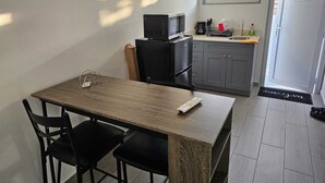 Kompakti keittiö, jossa on mikroaaltouuni, kahvinkeitin ja pesuallas. Keittiössä on ruokapöytä tuoleineen sekä pöydällä kaukosäädin.
