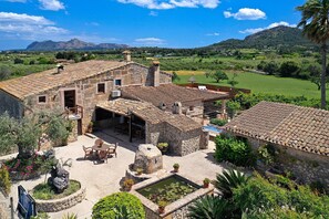 A stone building with a tiled roof, a courtyard with a fountain, and a view of a green landscape with mountains in the background. - Ca Sonaris, Finca 5StarsHome Mallorca (Alcúdia)