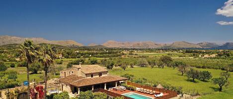 A villa with a swimming pool, surrounded by lush greenery and mountains in the background.