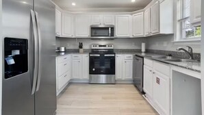 A modern kitchen with white cabinets, stainless steel appliances, and a granite countertop. - The Shell: Walk-to-Beach Retreat (Long Beach)