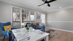 A dining area with a white table set for four, blue chairs, and a ceiling fan. - The Shell: Walk-to-Beach Retreat (Long Beach)