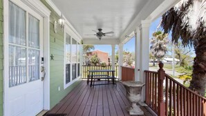 A covered porch with a ceiling fan, a wooden table with benches, and a stone planter. - The Shell: Walk-to-Beach Retreat (Long Beach)