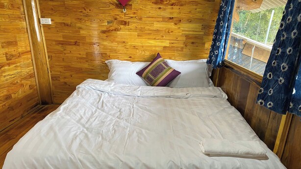 Una habitación de cabaña de madera con una cama, una ventana con cortinas y piso de madera.