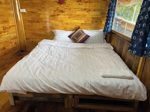Una habitación de cabaña de madera con una cama, una ventana con cortinas y piso de madera.