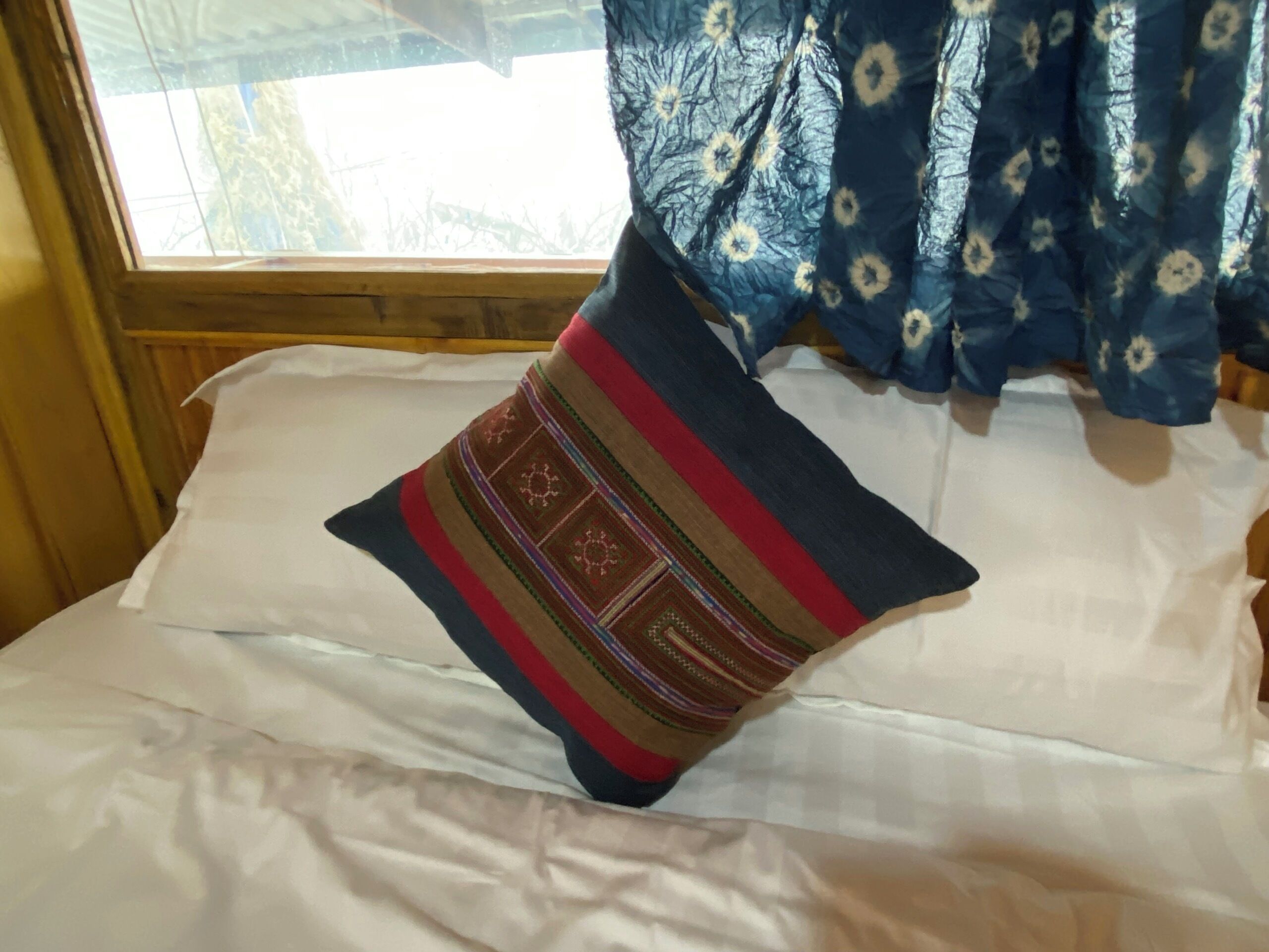 A bed with a white sheet and a decorative pillow with a geometric pattern.