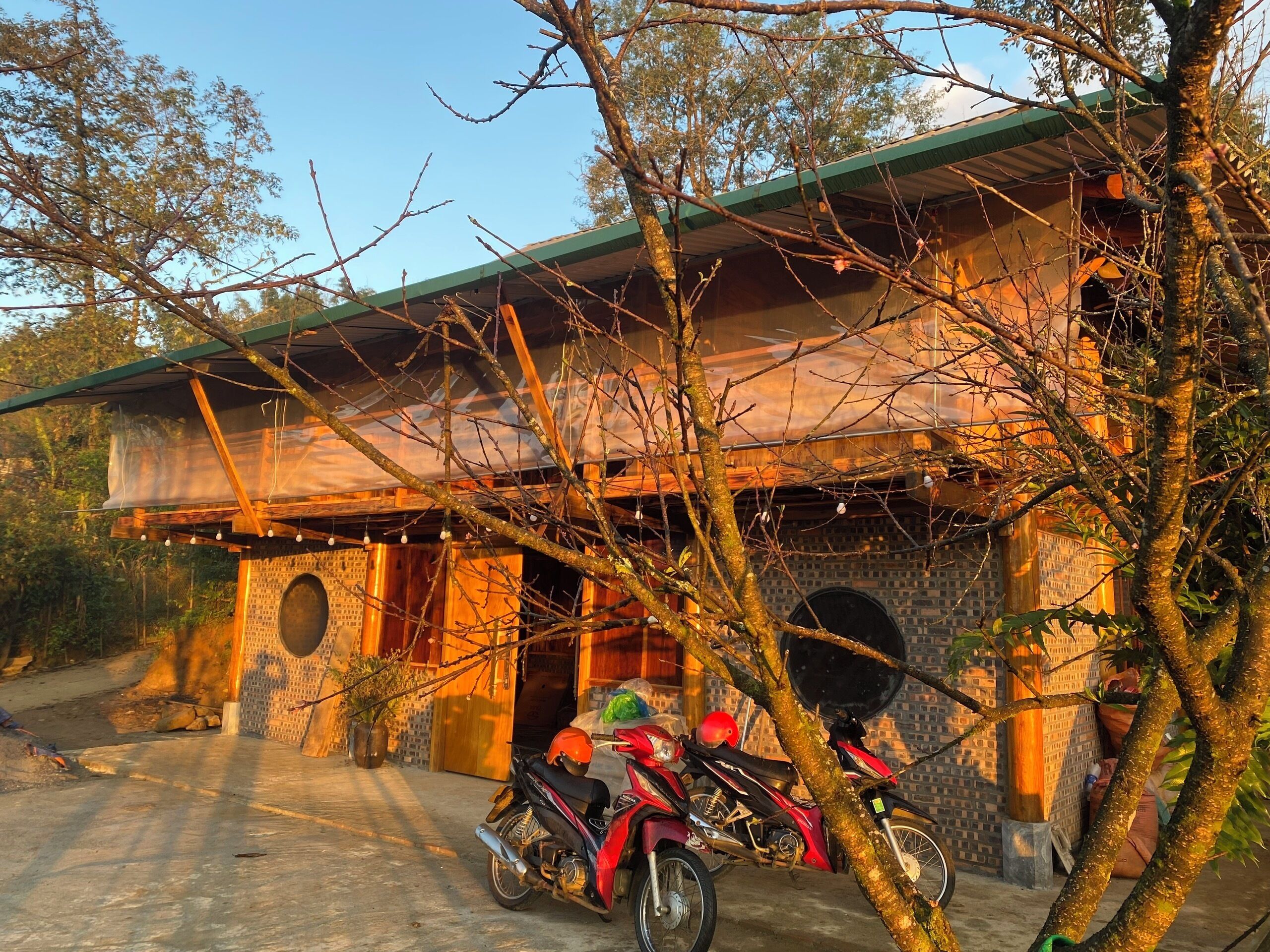 A rustic building with a green roof, a brick wall, and a wooden door. There are two motorcycles parked in front.