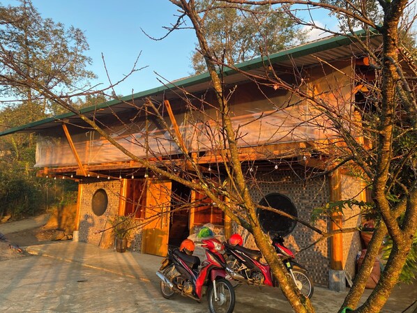 A rustic building with a green roof, a brick wall, and a wooden door. There are two motorcycles parked in front.