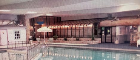 Una piscina interior con tabla de salto, sombrilla y un pequeño edificio contiguo a la piscina.