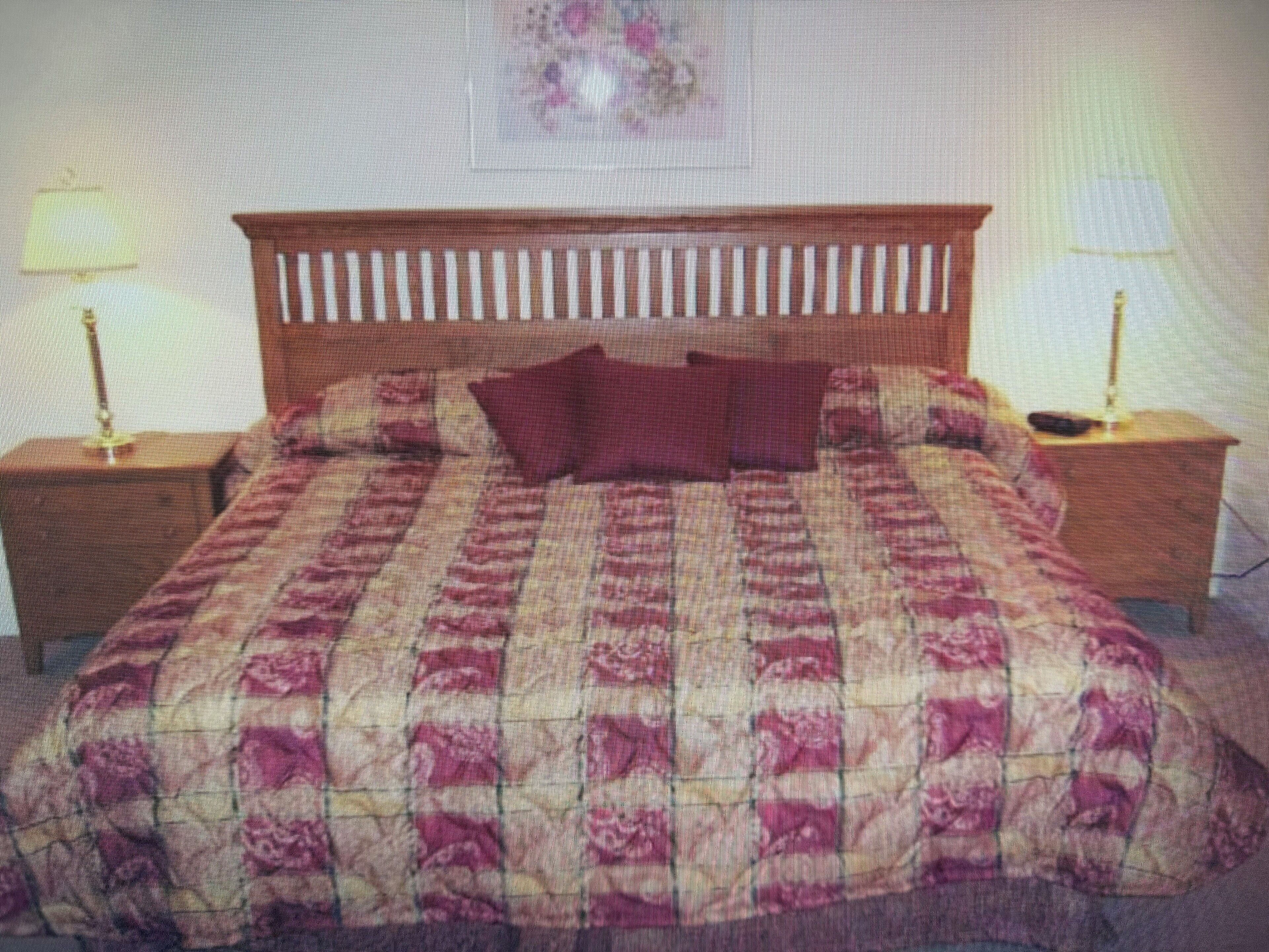 A bedroom with a wooden headboard, a patterned bedspread, two nightstands, and a lamp on each side.