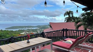 Un balcon avec une table et des chaises, offrant une vue panoramique sur la mer et les collines.