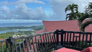 Une terrasse aux tuiles rouges, dotée d’une chaise longue et de coussins, qui offre une vue imprenable sur un paysage côtier, la mer et une île lointaine.
