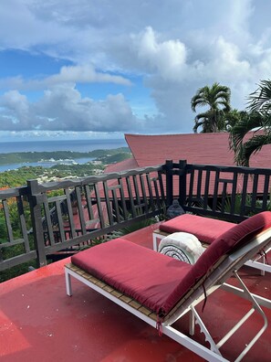 A balcony with a red roof, a white metal chair, and a red cushion. - Shibui Cove, your private retreat to recharge. (St Thomas)
