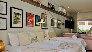 Une chambre d’hôtel avec deux lits, une télévision, des œuvres d’art au mur et une fenêtre donnant sur un paysage.