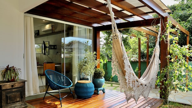 Une terrasse en bois avec un hamac, une chaise bleue et des plantes en pot.