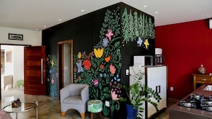 Une cuisine moderne avec un mur d’accent rouge, un fauteuil gris et une fresque murale aux motifs floraux et aux couleurs vives.