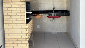 A brick-built outdoor kitchen with a built-in grill, a red sink, and a ceiling fan. - Spacious and comfortable apartment in a prime neighborhood in the city of Porto Seguro, Bahia. (Porto Seguro)