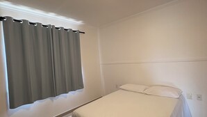 A bedroom with a single bed, a window with curtains, a ceiling light, and a white wall. - Spacious and comfortable apartment in a prime neighborhood in the city of Porto Seguro, Bahia. (Porto Seguro)