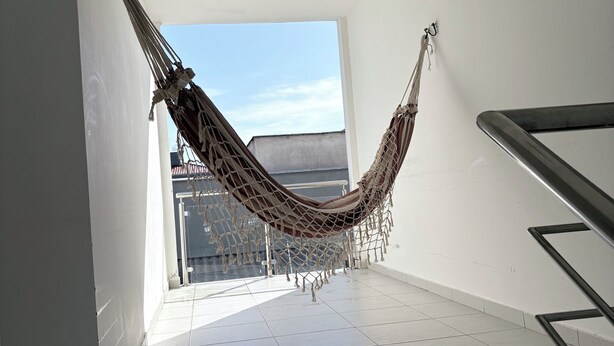 A hammock in a spacious, sunlit room with a view of buildings outside. - Spacious and comfortable apartment in a prime neighborhood in the city of Porto Seguro, Bahia. (Porto Seguro)