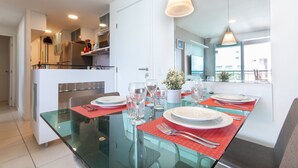 A modern dining area with a glass table set for four, red placemats, and a potted plant. - Ahead Ponta Negra #602 - Apartment by Carpediem (Natal)