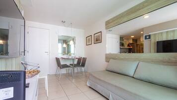 A modern living room with a sofa, a dining table with chairs, and a kitchen area in the background.