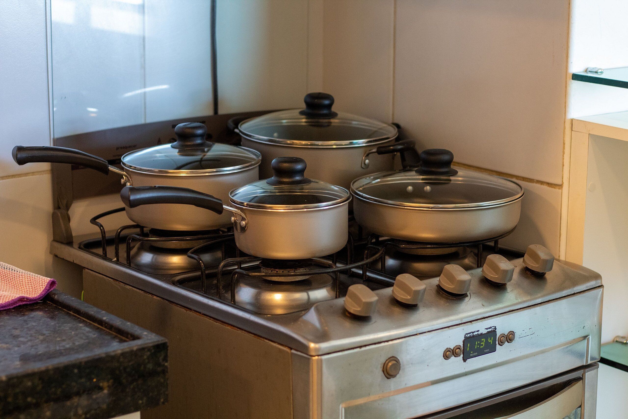 A stainless steel stove with four pots on burners and a digital clock displaying 11:34.