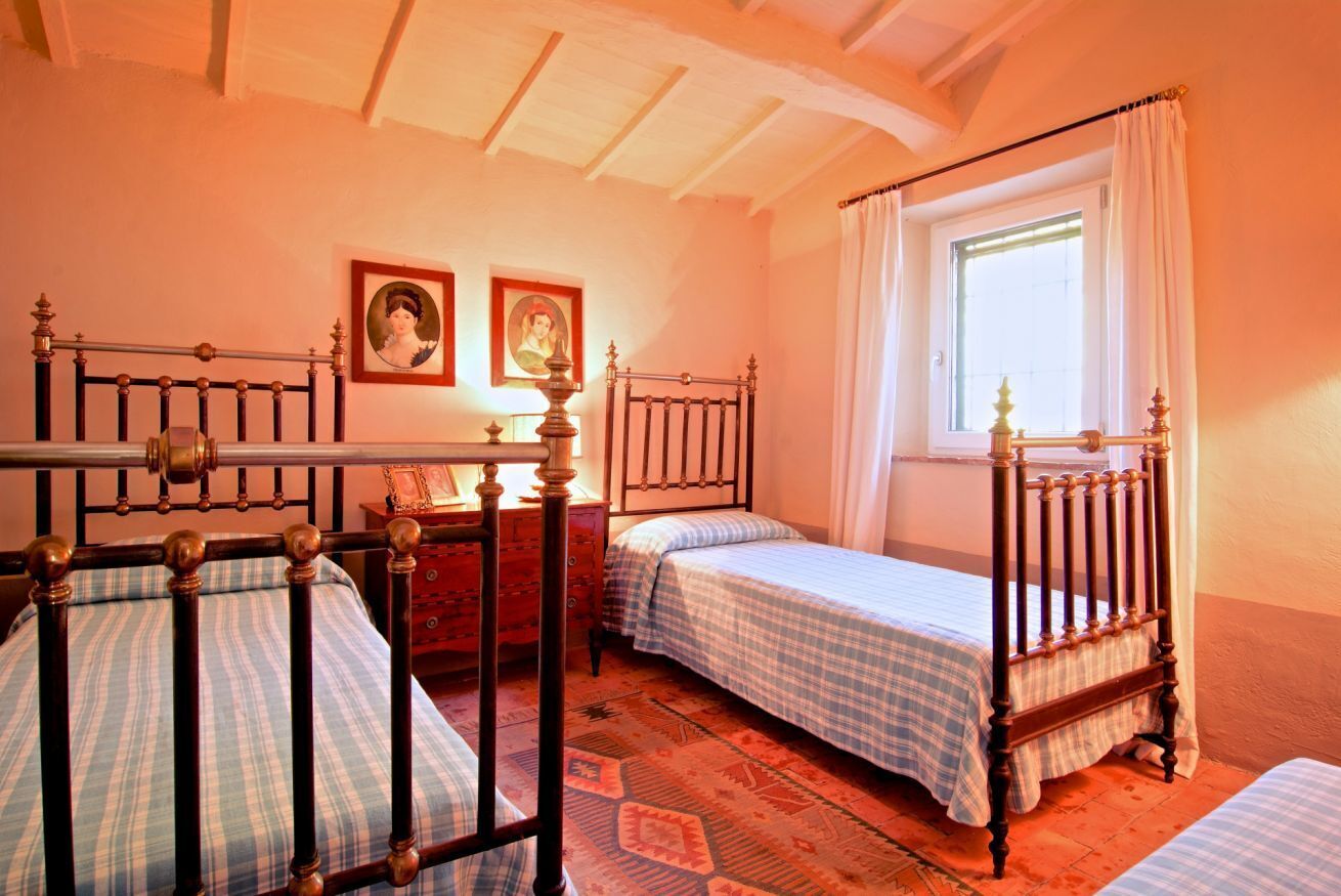 Une chambre à coucher avec deux lits en bois, une fenêtre avec des rideaux et deux tableaux encadrés accrochés au mur.