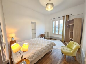 A bedroom with a bed, bedside lamps, a chair, a wardrobe, and a window with a view.