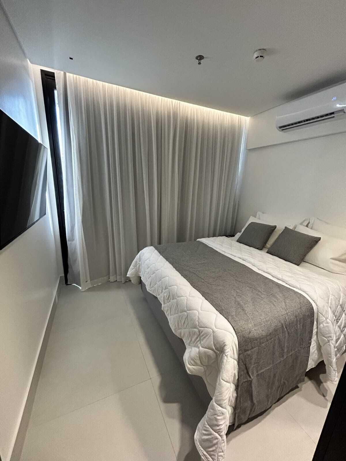 Un dormitorio moderno con una cama grande, un televisor de pantalla plana montado en la pared y un equipo de aire acondicionado.