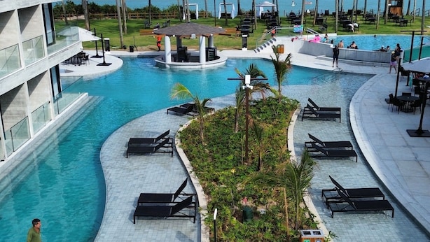 Et resortområde med flere swimmingpools, liggestole og palmer.