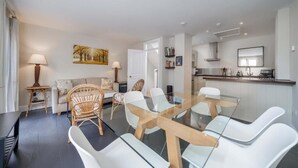 Ein modernes Wohnzimmer mit einem Esstisch mit Glasplatte, weißen Stühlen und einem Sofa mit einem blumigen Kissen.