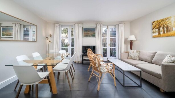 Ein modernes Wohnzimmer mit einem Glastisch, weißen Stühlen, einem beigen Sofa und einem Kamin.