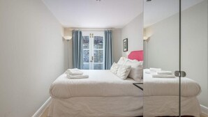 Ein Schlafzimmer mit einem großen Bett, einem Fenster mit Vorhängen und einem Spiegel.