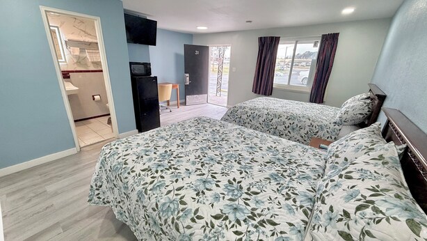 A hotel room with two beds, a TV, a small desk, and a bathroom visible through an open door. - Deluxe Inn (Wilson)