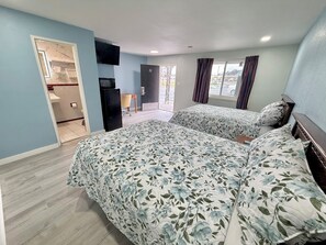 A hotel room with two beds, a TV, a small desk, and a bathroom visible through an open door.
