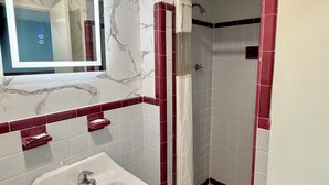A bathroom with a marble wall, a white sink, and a glass-enclosed shower. - Deluxe Inn (Wilson)