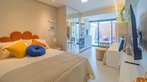 Une chambre moderne avec un grand lit, un bureau et une télévision. Elle dispose d’un balcon avec vue sur l’extérieur.