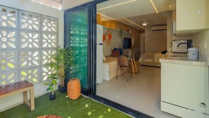 Un appartement moderne doté d’une porte en verre donnant sur un espace de vie, une cuisine et un balcon agrémenté de gazon synthétique et de plantes en pot.