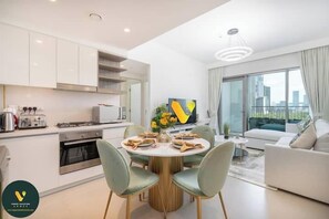 A modern kitchen with white cabinets, a dining table with chairs, and a large window with a city view. - Vogue | Downtown with Direct Access to Dubai Mall (Dubai)