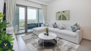 A modern living room with a white sofa, a round coffee table, and a large sliding glass door leading to a balcony. - Vogue | Downtown with Direct Access to Dubai Mall (Dubai)